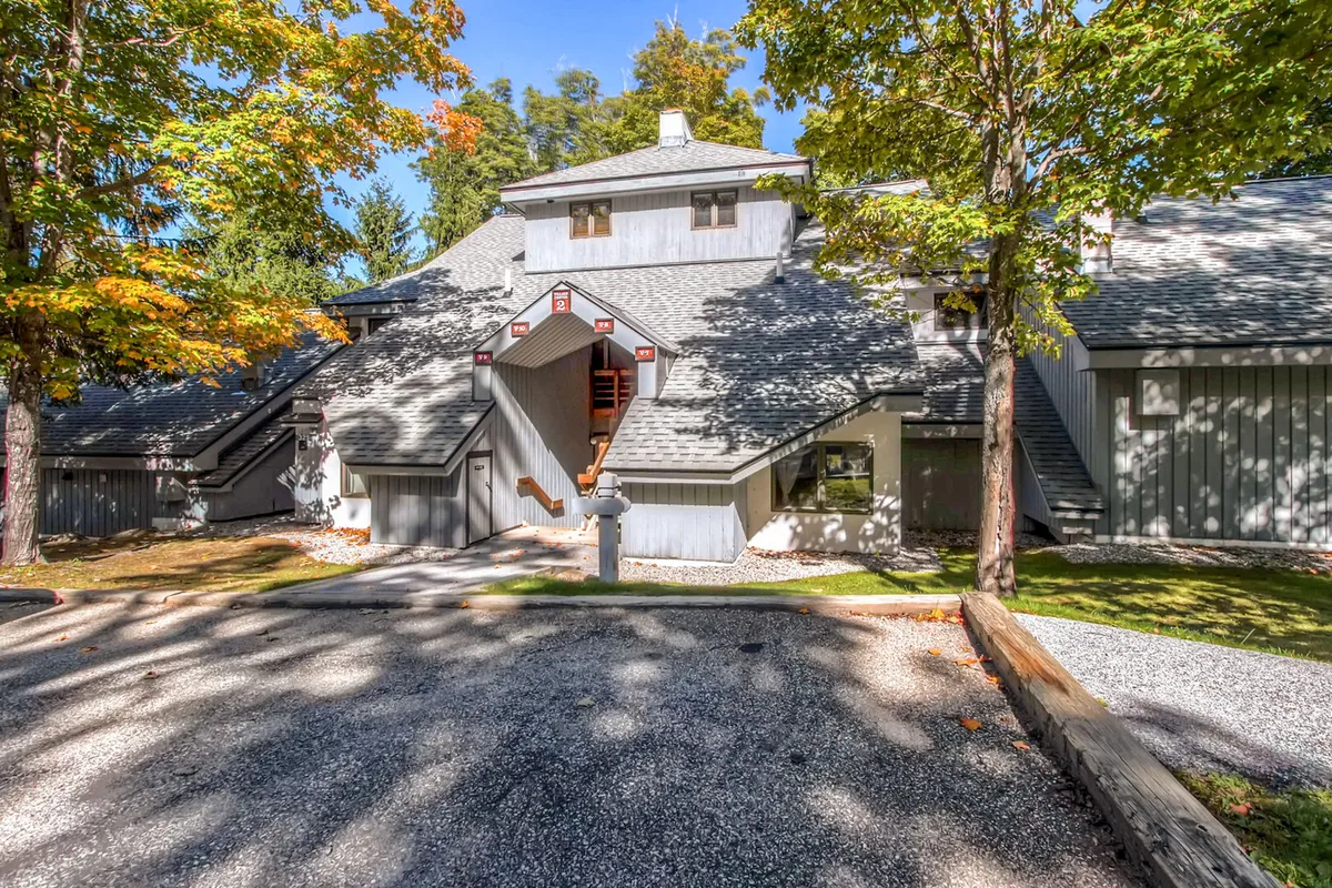 This exterior image features the architectural details of the building surrounded by mature trees, with a driveway leading to the entrance. The inviting and serene scene evokes a sense of arrival, relaxation, and connection to nature—ideal for families returning after a day of adventure.