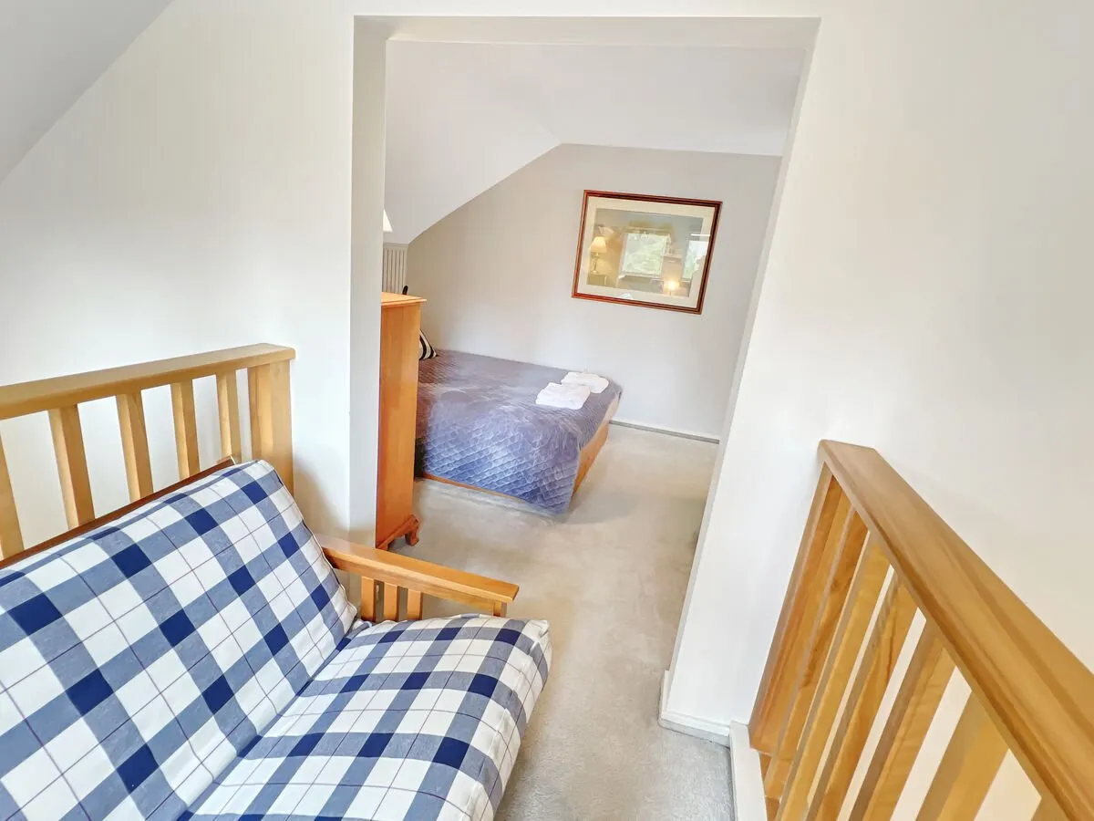 A loft-style area with a plaid sofa, bed covered in a blue quilt, and framed artwork. The shared, versatile space blends sleeping and lounging, making it perfect for children, teens, or friends to relax or socialize.