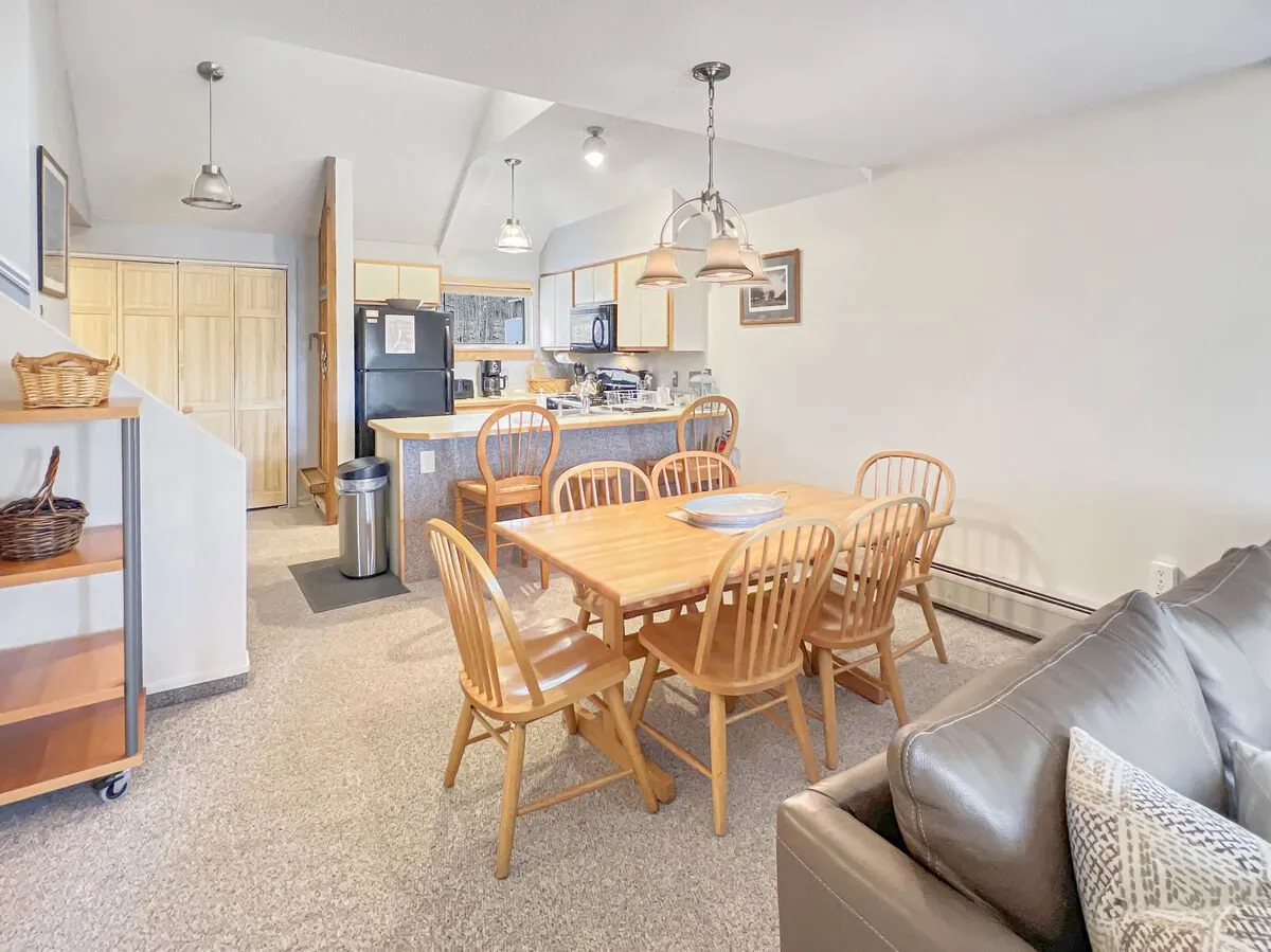 A welcoming open-concept dining and kitchen area with a large dining table surrounded by chairs, seamlessly adjacent to a fully equipped kitchen and a comfortable seating nook. The space is filled with natural light, and the setup is perfect for shared meals or casual gatherings.