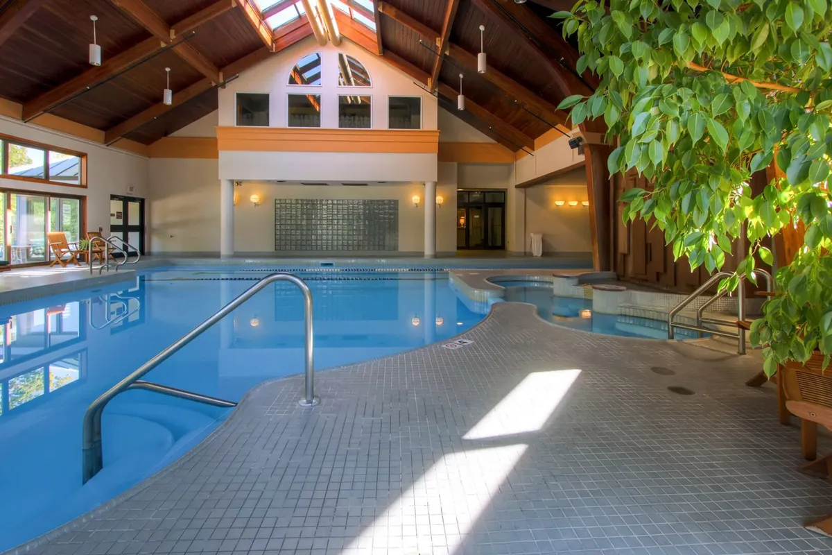 An inviting indoor swimming pool area with skylights and lush indoor plants, creating a rejuvenating and light-filled space. The setting is serene, ideal for relaxation, wellness activities, and shared moments for couples.