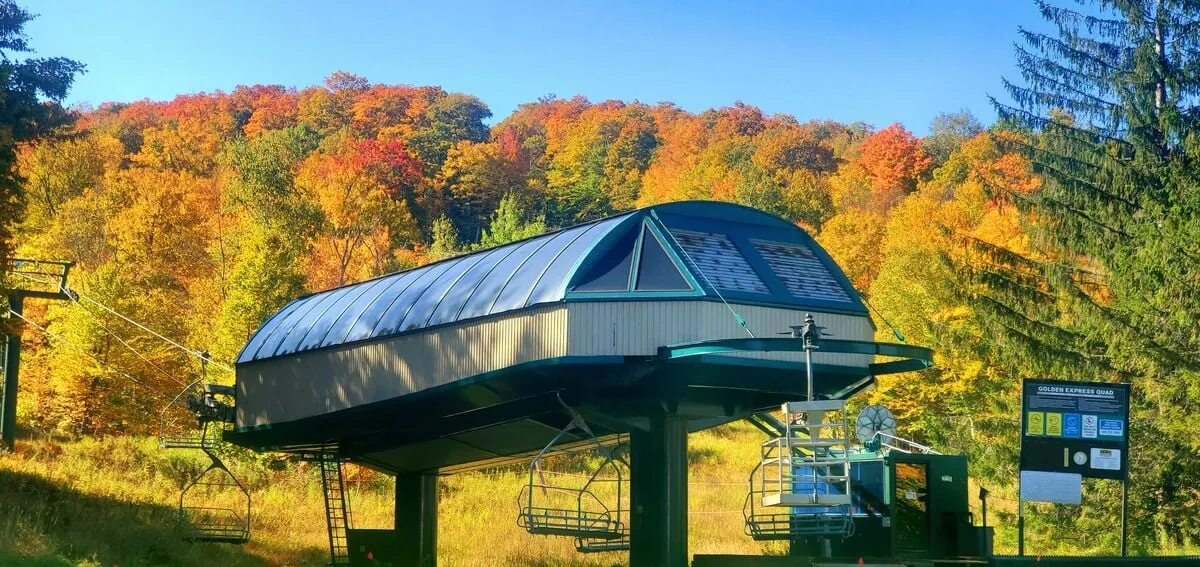 An exterior scene showcases a ski lift station set against vibrant autumn foliage, with clear signage and a family-friendly, adventurous ambiance. The natural beauty and accessibility to outdoor activities are evident.