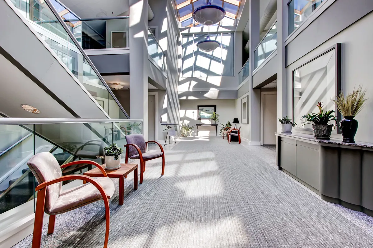 A stylish lounge area with elegant chairs, decorative plants, a modern side table, and a large skylight pouring in natural daylight. The space is ideal for unwinding, socializing with a glass of wine, or enjoying a light meal from the café or wine bar.
